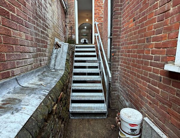Galvanised open-tread steel staircase installed between brick walls